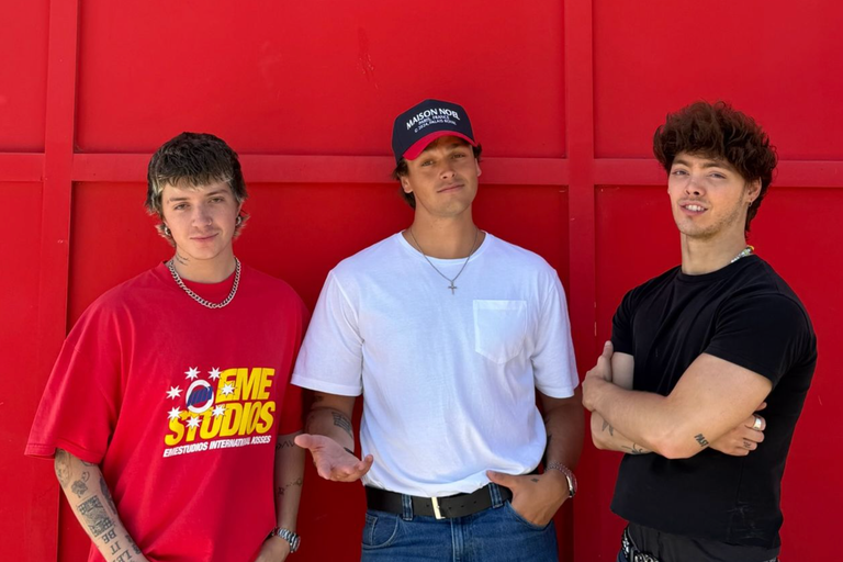 Promotional portrait of Jonah Marais, Jack Avery, and Zach Herron posing casually against a bright red background.
